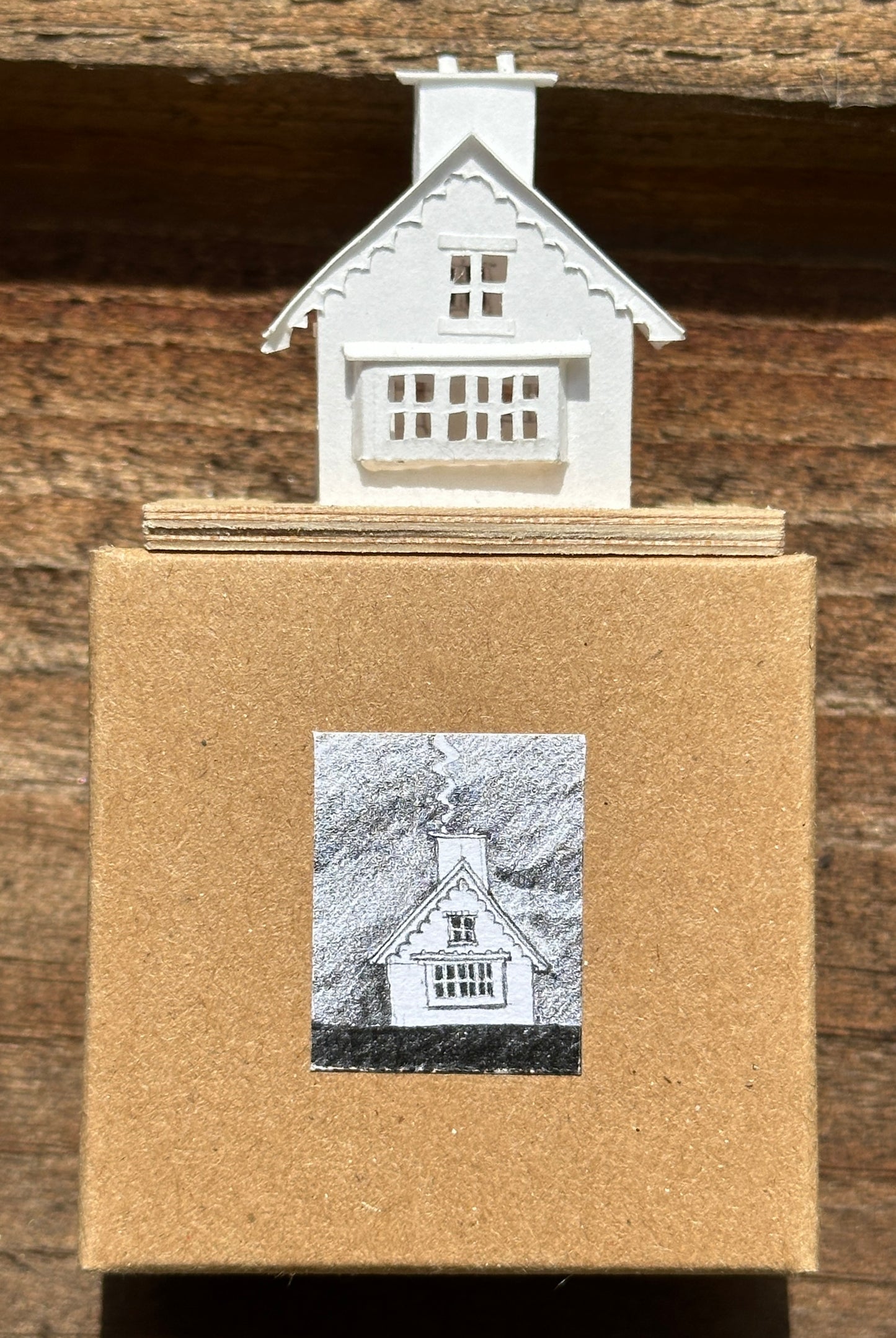 white paper gable fronted house with double chimney on plywood base  above presentation box