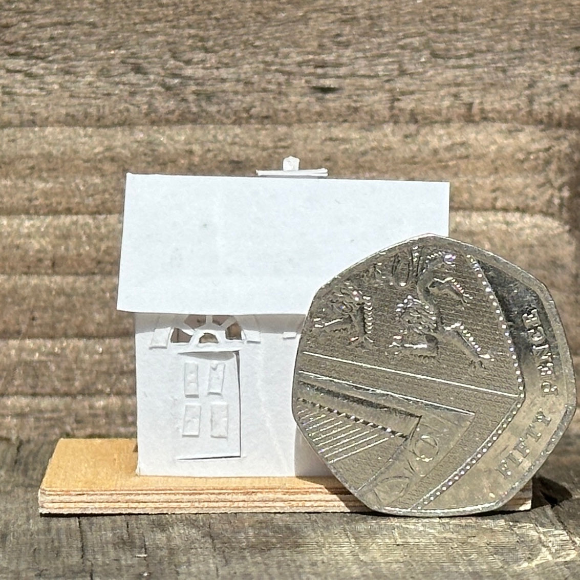 white paper house with arched windows on plywood base with 50p for scale
